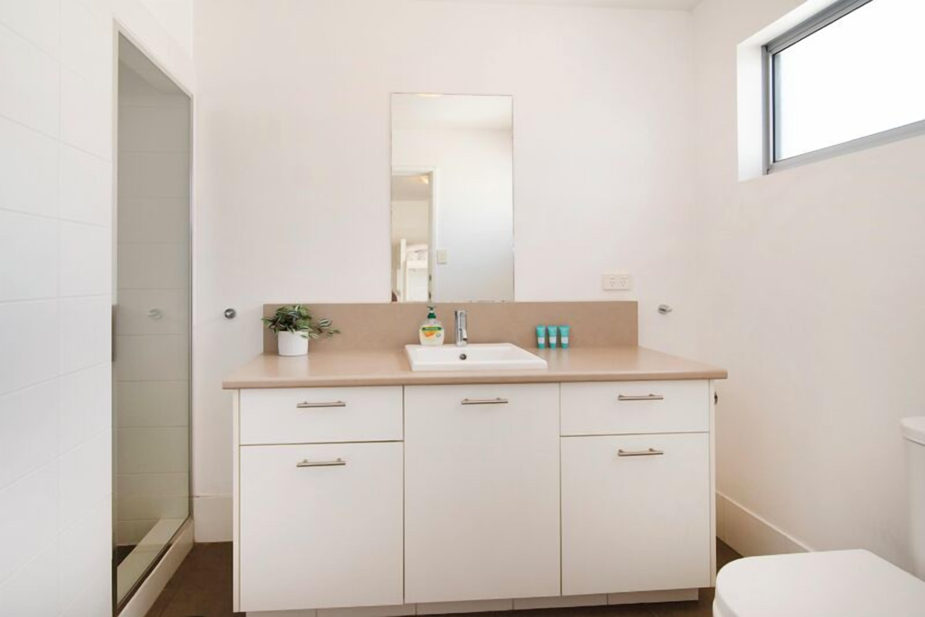 A bathroom with a white sink, mirror, and cabinets.