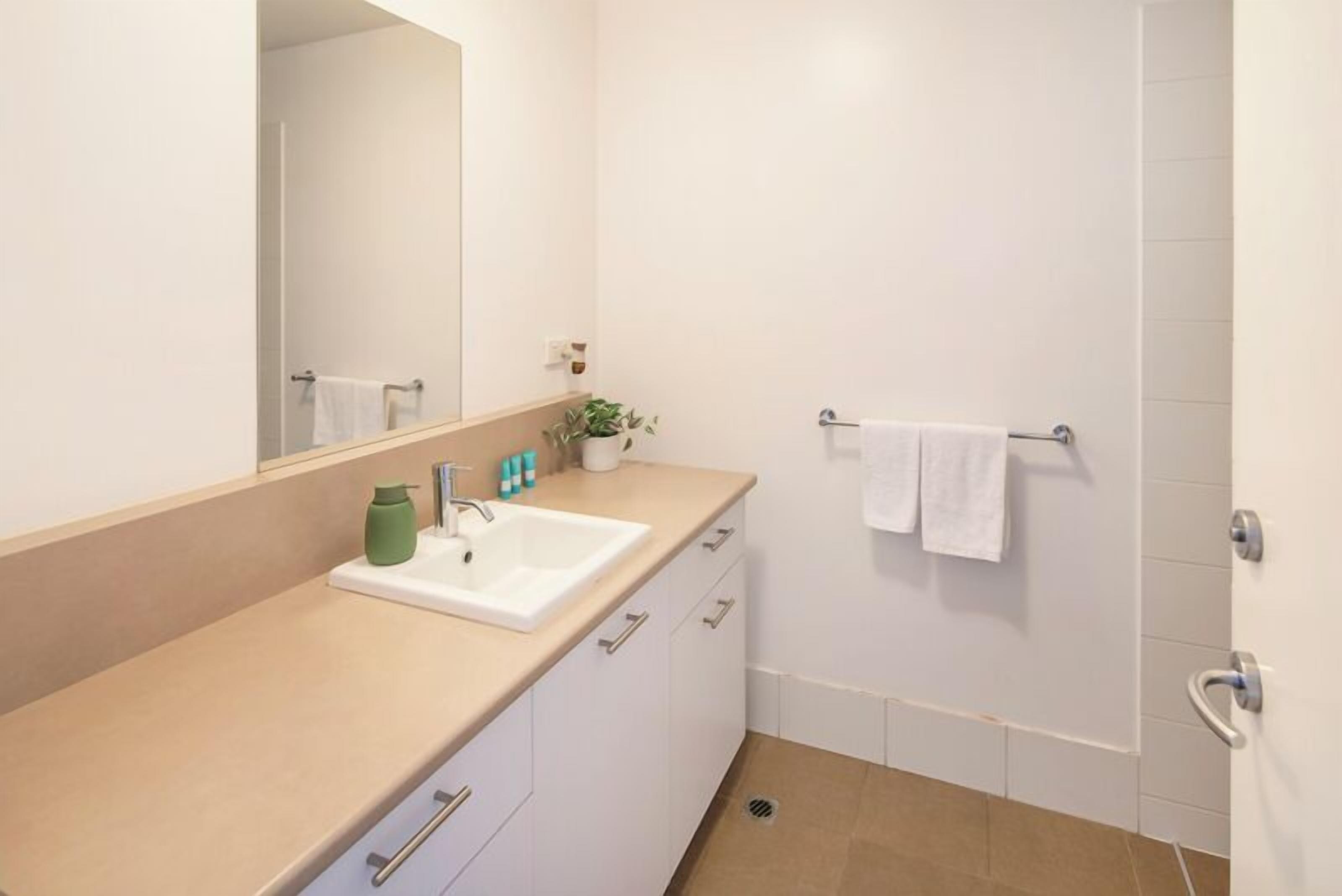 Een moderne badkamer met een beige aanrechtblad, witte kastjes, een grote spiegel, een wastafel, een handdoekhouder en een potplant.