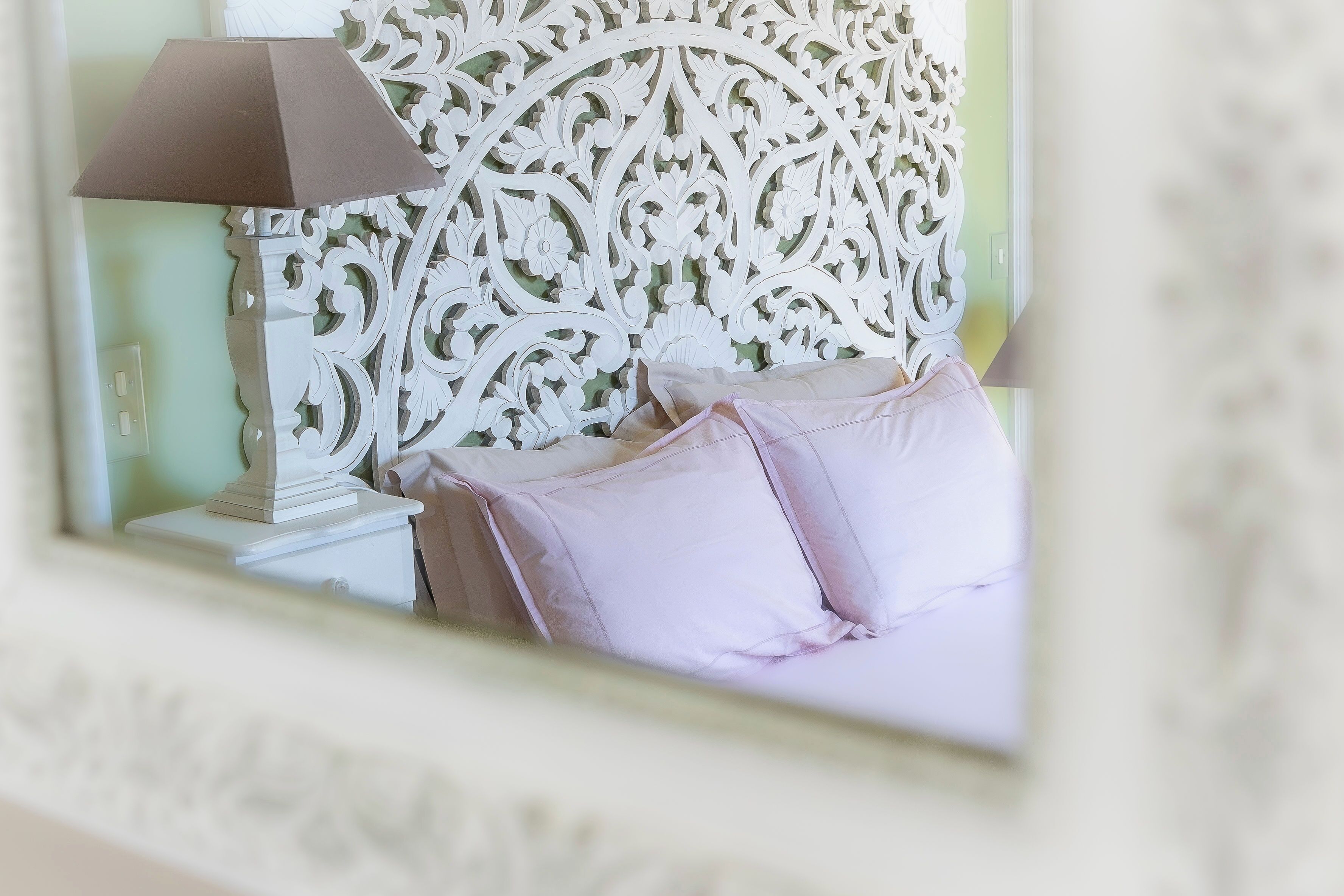Une chambre à coucher avec une tête de lit décorative, une lampe de chevet et un lit agrémenté d’oreillers roses.