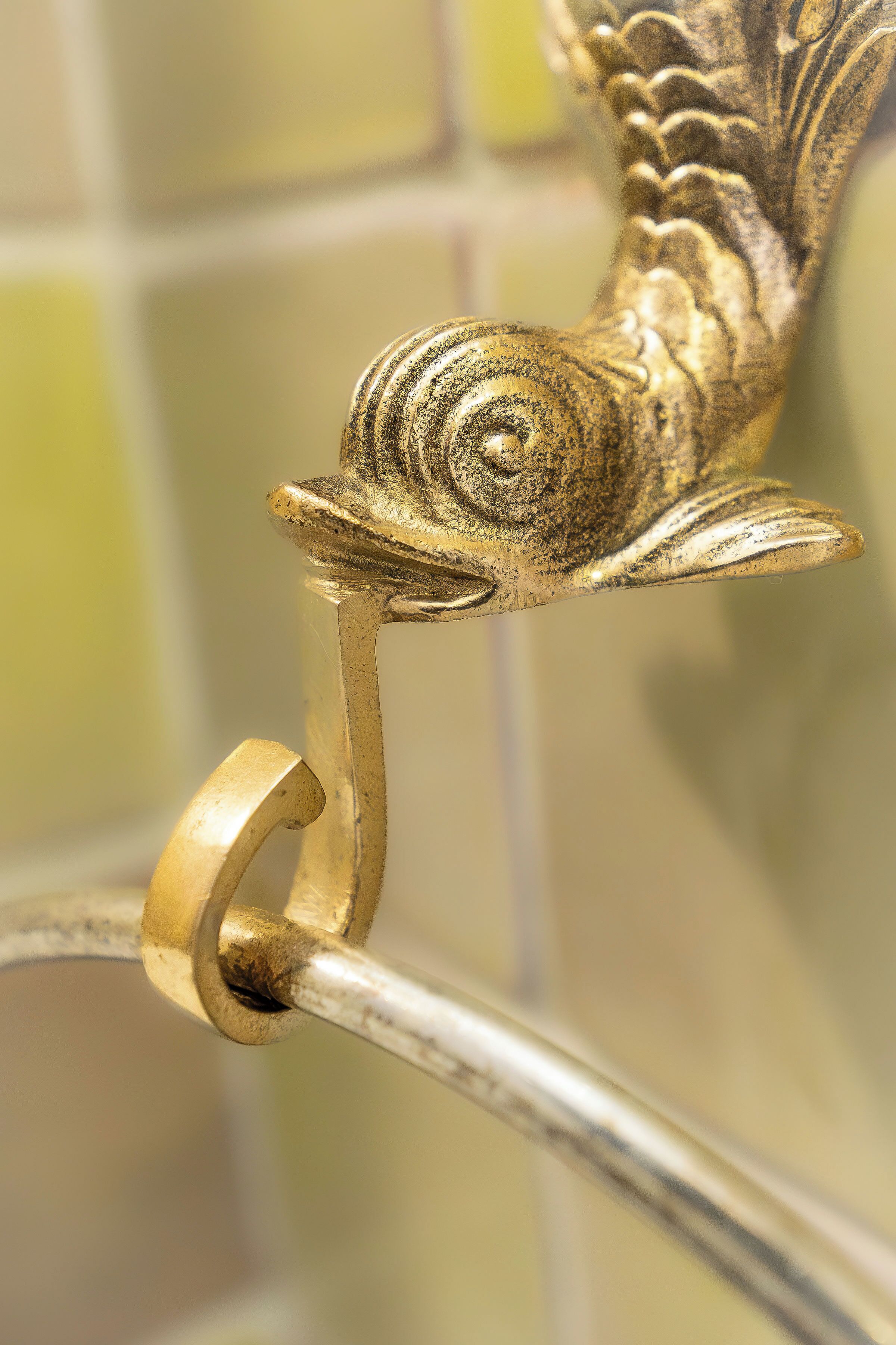A close-up of a brass fish-shaped handle on a metal fixture.