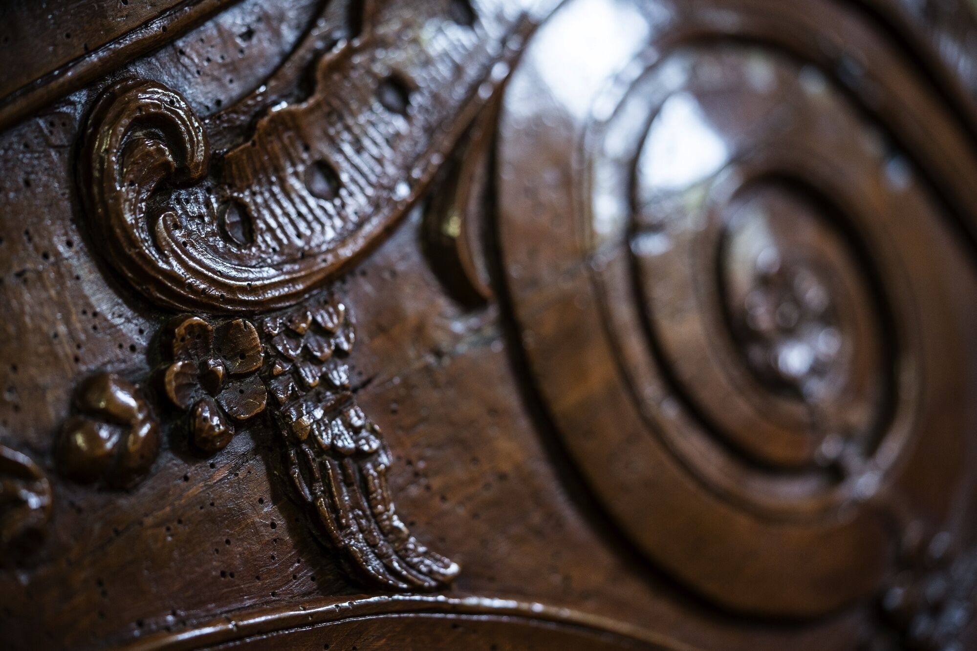 A close-up of a wooden surface with intricate carvings, including floral and spiral designs.