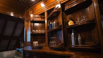 Una zona de bar con estanterías de madera, botellas, vasos y un lavamanos de metal.