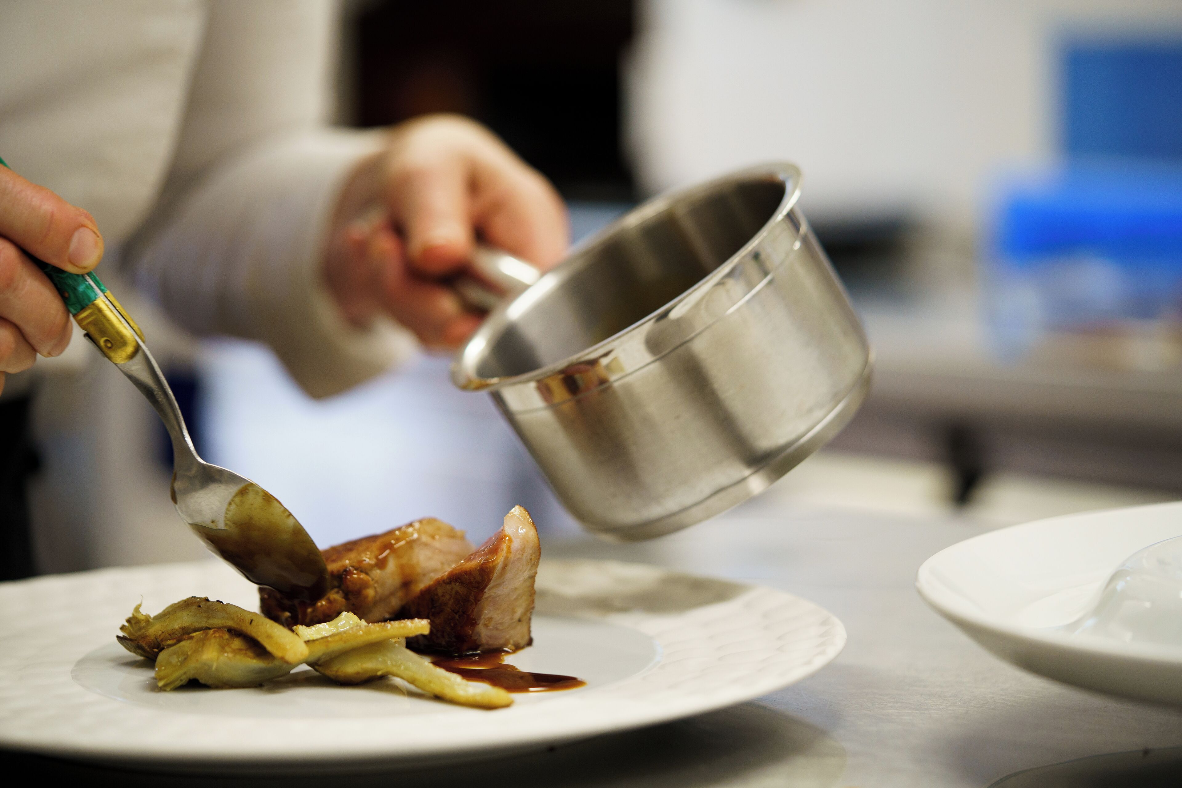 A person pouring sauce from a metal container onto a plate with food.