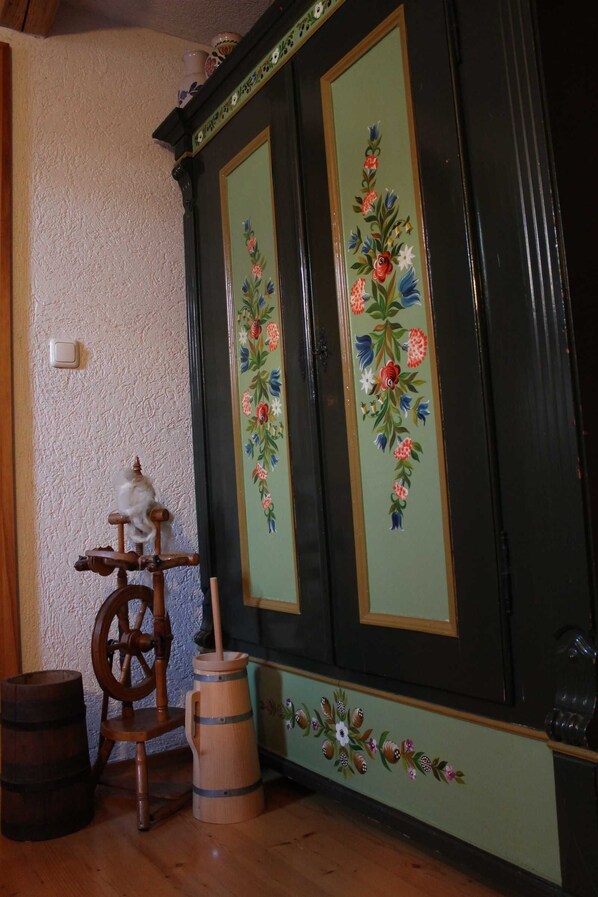 A room with a wooden barrel, a spinning wheel, and a cabinet with floral designs.