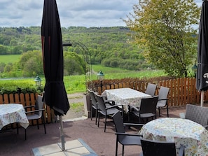 An outdoor patio with tables and chairs, surrounded by a wooden fence, overlooking a lush green landscape. - Vacation apartment Landidylle (Birx)