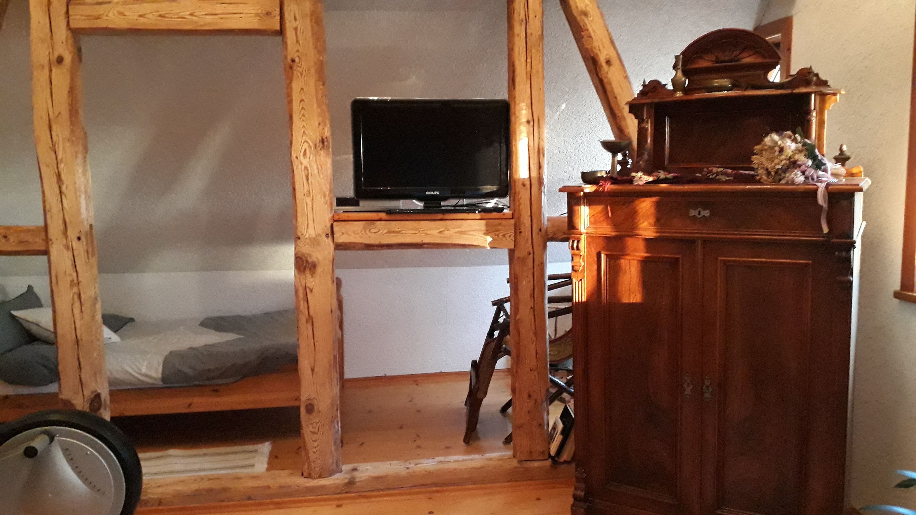 Une pièce avec des murs en bois, comprenant un lit, un téléviseur posé sur une étagère en bois et un meuble.