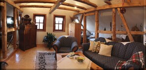 A cozy living room with wooden beams, a sofa, a chair, a television, and a cabinet.