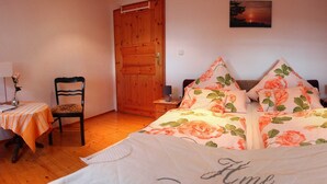 Een slaapkamer met een bloemenbedekking, een houten garderobe en een klein tafeltje met een stoel.