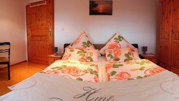 Une chambre à coucher avec une couvre-lit à motifs floraux, une armoire en bois et une petite table avec une chaise.