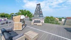 Eine Dachterrasse mit Korbmöbeln, einem Schornstein und Blick auf das Meer.