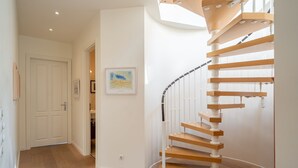 Eine Wendeltreppe mit Holzbodenstufen und weißen Geländern in einem Flur mit Holzdielen und weißen Wänden.