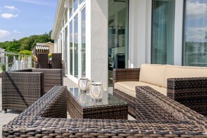 An outdoor seating area with wicker furniture and a glass-top table, overlooking a modern building with large windows. - Baltic Sea Domicile Bansin, App. 4.1 (Heringsdorf)