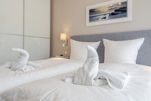 A hotel room with two beds, each with neatly folded towels, a bedside lamp, and a framed picture on the wall.