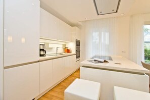 A modern kitchen with white cabinetry, a central island, and a dining area with white chairs. - Beach residences Bansin, Ostseepalais 01 (Heringsdorf)