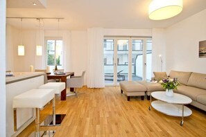 A modern living room with a sofa, ottoman, and a dining area with a table and chairs. - Beach residences Bansin, Ostseepalais 01 (Heringsdorf)