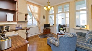 Uma sala de estar com sofá, televisão, mesa de centro de madeira e uma área de cozinha com micro-ondas e torradeira.