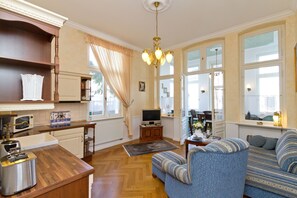 Ein Wohnzimmer mit einer Couch, einem Fernseher, einem Holztisch und einer Küchenzeile mit Mikrowelle und Toaster.