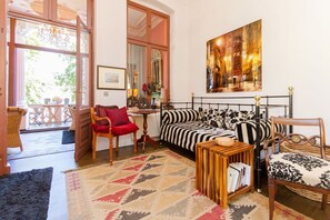 Um quarto aconchegante com uma cama, uma mesinha de madeira, uma cadeira, um tapete estampado e uma janela grande.