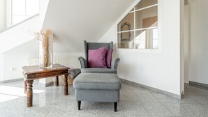 Un interior moderno con un sillón tapizado gris, una mesita de madera y un jarrón con plantas secas.