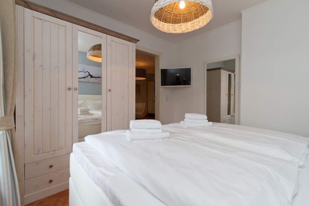 A bedroom with a large bed, a wardrobe, a television, and a wicker light fixture.