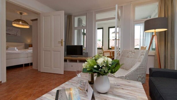 Ett modernt vardagsrum med en soffa, ett soffbord med en vas med blommor, en tv och en fåtölj.