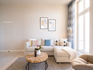 Ein modernes Wohnzimmer mit einem beigen Sofa, einem runden Couchtisch mit Blumenvase und zwei gerahmten Kunstwerken an der Wand.