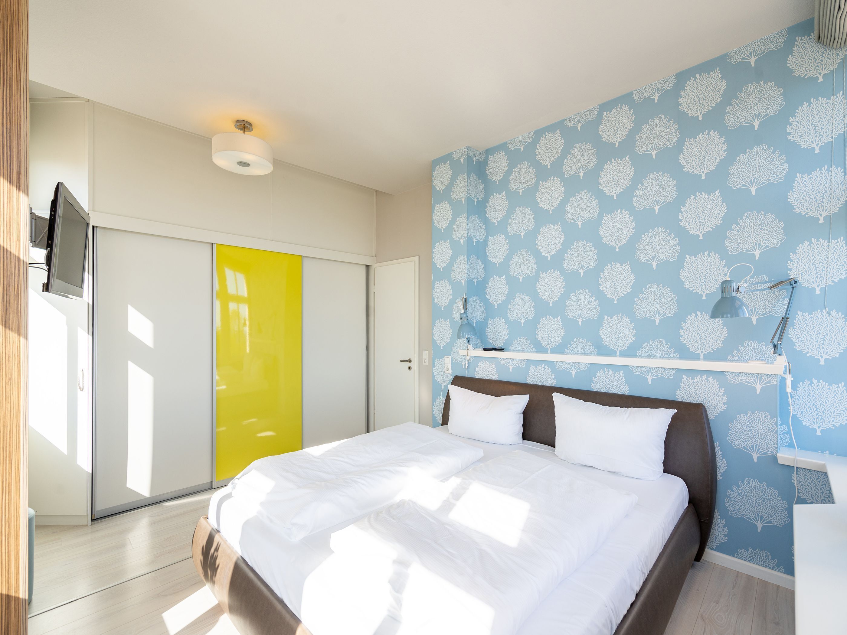 Un dormitorio con cama, armario, escritorio y pared con diseño de árbol.
