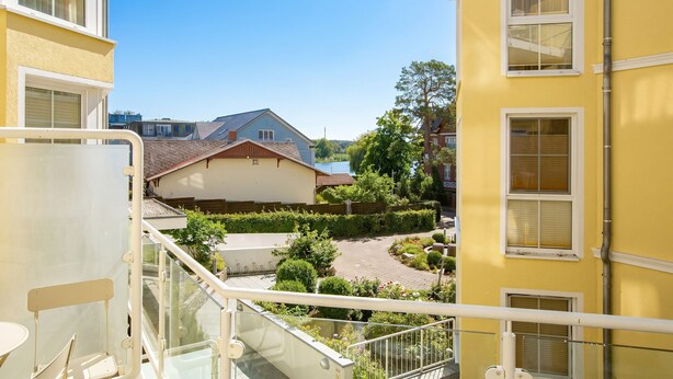 Ein Wohngebäude mit Balkon, freiem Blick auf ein Nachbarhaus und einem gepflegten Garten.