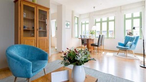 Un salon moderne avec un fauteuil bleu, un meuble en bois, une table à manger avec des chaises et un vase rempli de fleurs.