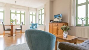Un salon moderne comprenant un coin repas, de grandes fenêtres, un téléviseur et un vase de fleurs.