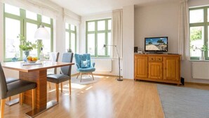 Un salon moderne avec une table à manger en bois, des fauteuils bleus et un téléviseur posé sur un meuble en bois.