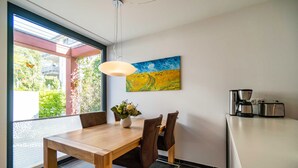 Et moderne spiseområde med et træbord, brune stole, en vase med blomster, et billede på væggen og en køkkenhalvø med hårde hvidevarer.