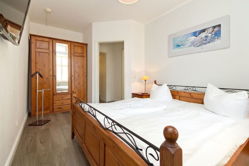 A bedroom with a wooden bed, a nightstand with a lamp, and a painting on the wall.