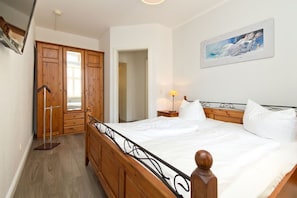 A bedroom with a wooden bed, a nightstand with a lamp, and a painting on the wall. - Villa Frisia, App. 19 (Heringsdorf)
