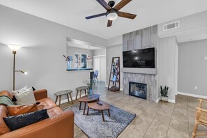 A modern living room with a leather sofa, a coffee table, a fireplace, and a TV mounted on the wall.