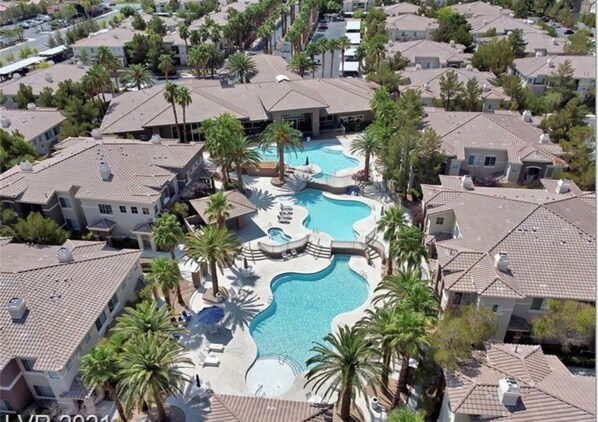 A residential area with a central swimming pool surrounded by houses and palm trees.