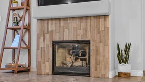 A modern living room with a wooden fireplace, a wooden ladder, and a potted plant.