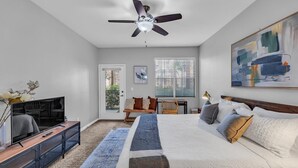 A bedroom with a bed, a desk, a television, and a ceiling fan.