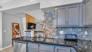 A modern kitchen with grey cabinets, a black countertop, and patterned backsplash tiles.