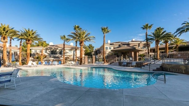 A swimming pool surrounded by palm trees and lounge chairs, with a building in the background.