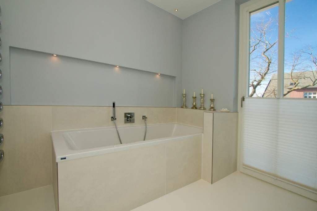 Un baño moderno con una bañera grande, una ventana con persianas y vista a un árbol.