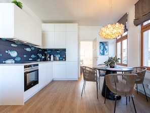 Une cuisine moderne avec des meubles blancs, un pare-feu bleu orné de motifs de poissons, et un coin repas avec des chaises en osier et une table ronde.