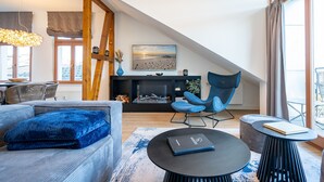 A modern living room with a loft-style ceiling, a fireplace, a blue armchair, and a round coffee table. - Villa Linquenda, App. 6 (Heringsdorf)