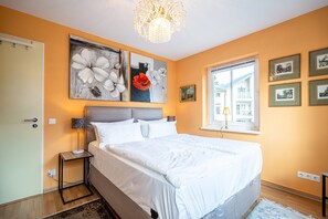 A bedroom with a large bed, a nightstand, a chandelier, and artwork on the walls. - Inselstrand, App. 314 (Heringsdorf)