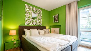 A bedroom with a bed, a nightstand with a lamp, a decorative mirror, a framed picture, and a window with curtains. - Inselstrand, App. 314 (Heringsdorf)