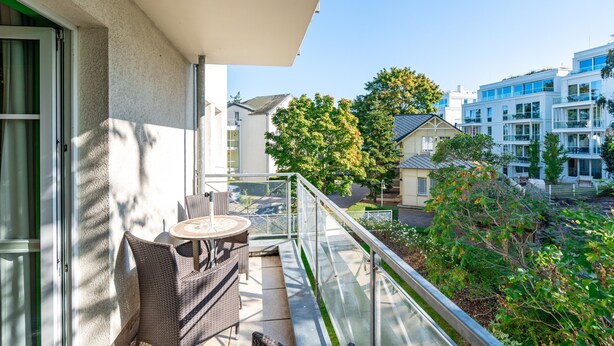 A balcony with wicker furniture, a glass railing, and a view of neighboring buildings and trees. - Inselstrand, App. 314 (Heringsdorf)