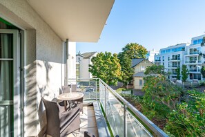 A balcony with wicker furniture, a glass railing, and a view of neighboring buildings and trees. - Inselstrand, App. 314 (Heringsdorf)