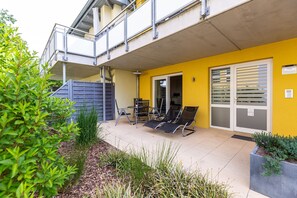 Un’area patio all'aperto con un muro giallo, una zona salotto coperta con sedie e un tavolo, e una scala che conduce a un livello superiore.