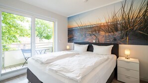 Ett modernt hotellrum med en stor säng, ett nattduksbord med en lampa, ett fönster med utsikt över grönområden och en tavla på väggen.