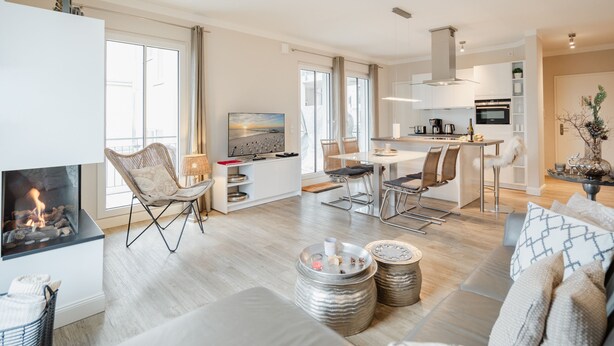 A modern living room with a fireplace, a dining area with a TV, and a kitchen with a bar.